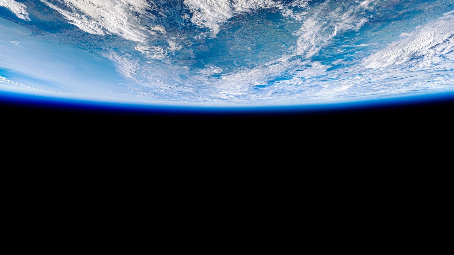 Vast view of Earth from space, showcasing clouds and the curvature of the planet against a dark background.